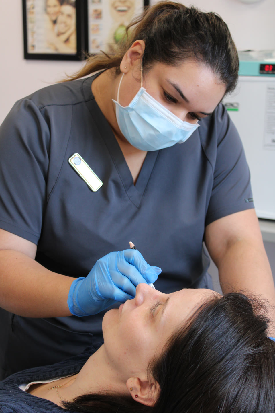 Dental professional in grey scrubs and blue gloves marking a patient's face with a pencil during a clinic procedure
