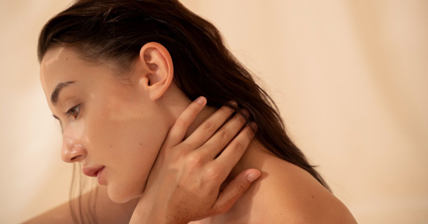 Woman in profile view touching her neck and jawline, showing a soft jaw definition against a neutral background
