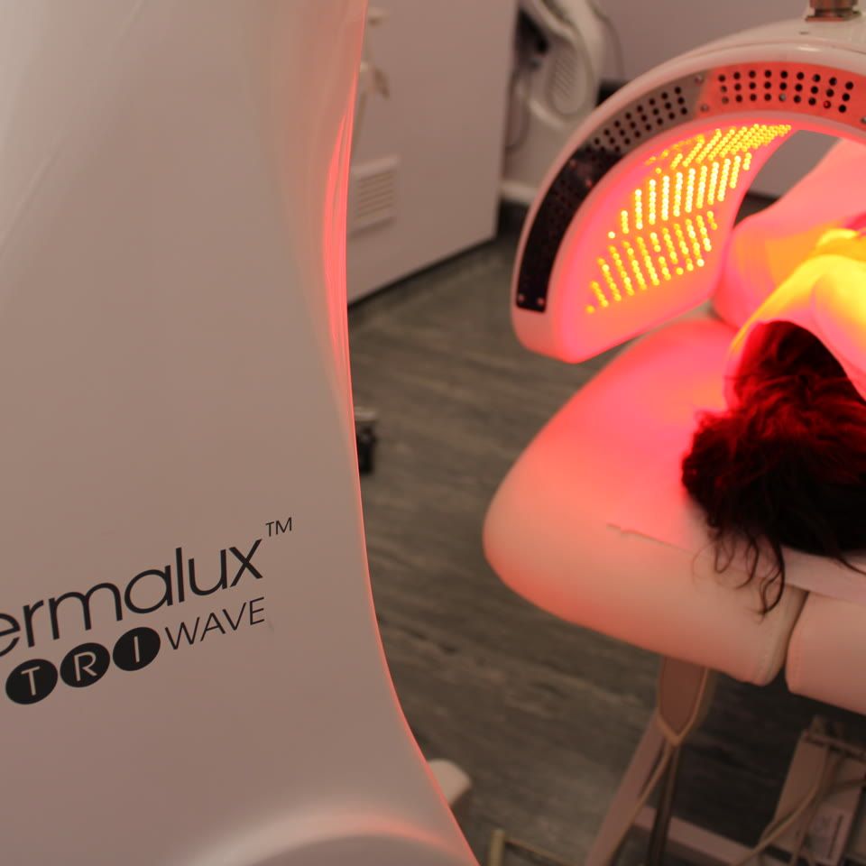 Client lying under a Dermalux TriWave LED light therapy device emitting red and near-infrared light during a treatment