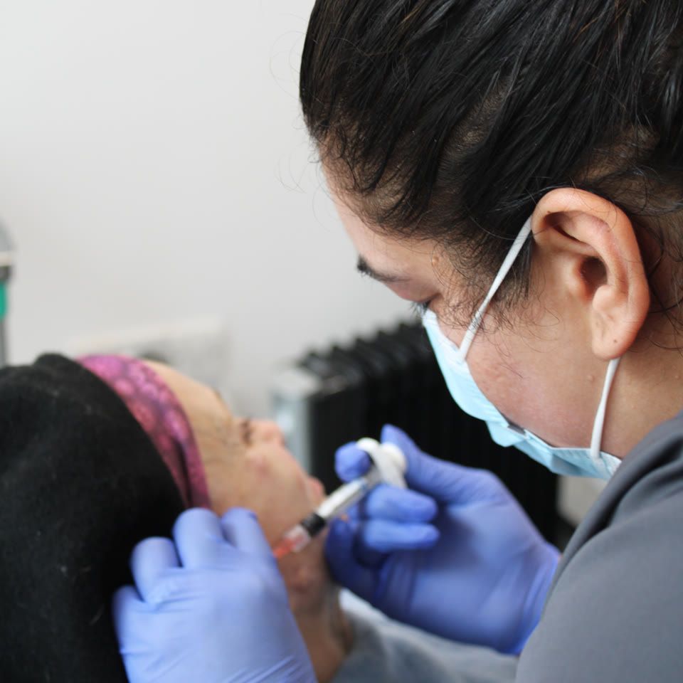Practitioner wearing gloves and a face mask administering a facial treatment to a client lying on a treatment bed