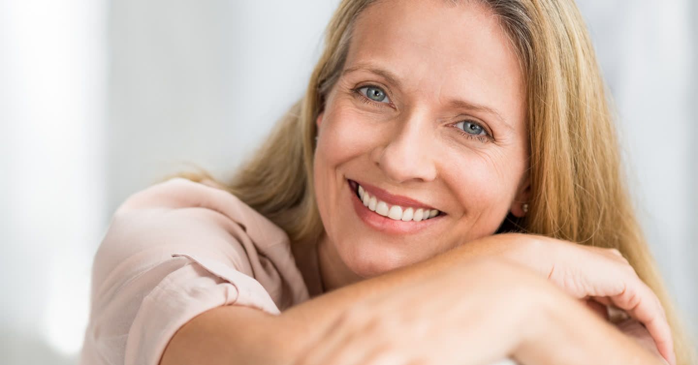 Smiling mature woman with blonde hair and blue eyes resting her chin on her folded arms