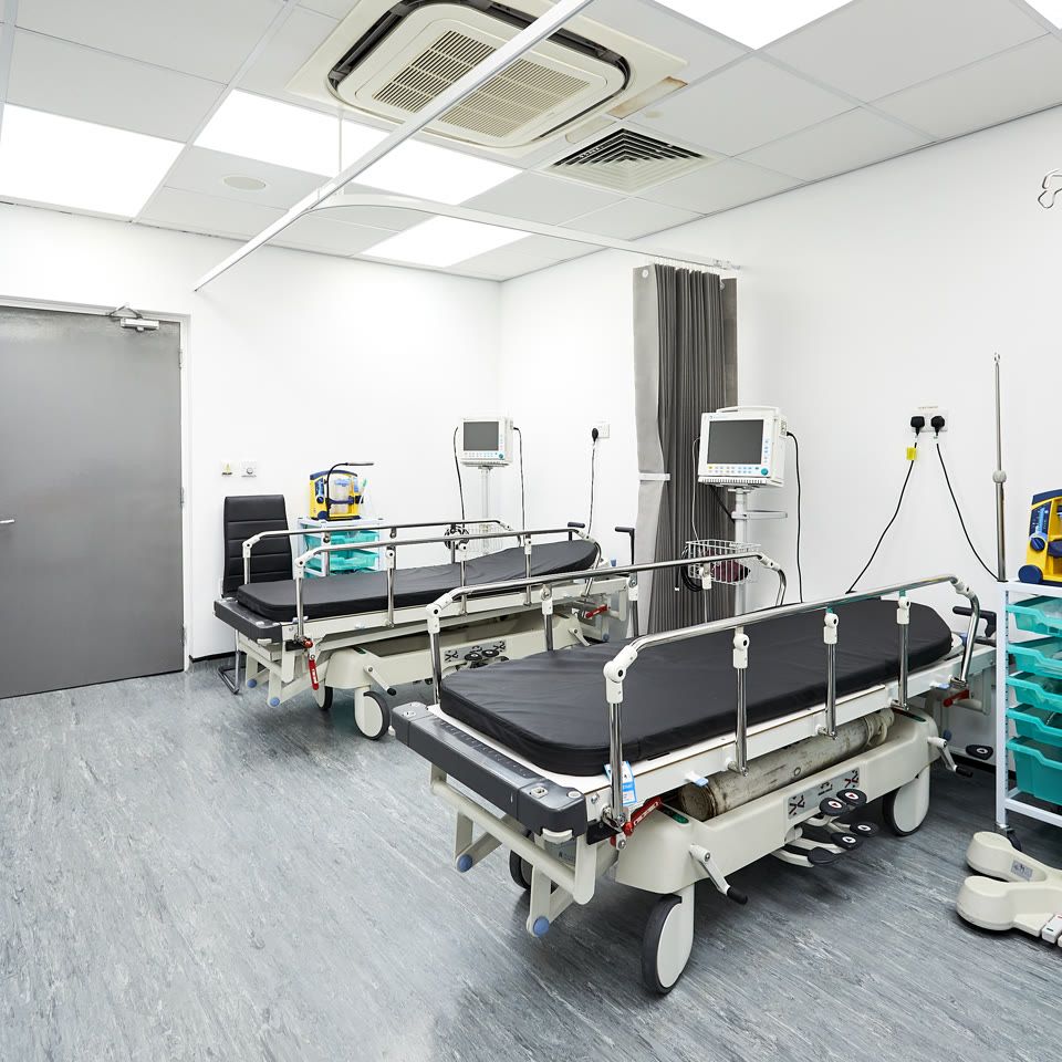Clinical treatment room with two hospital trolleys, patient monitors, IV stand, and medical equipment trolleys