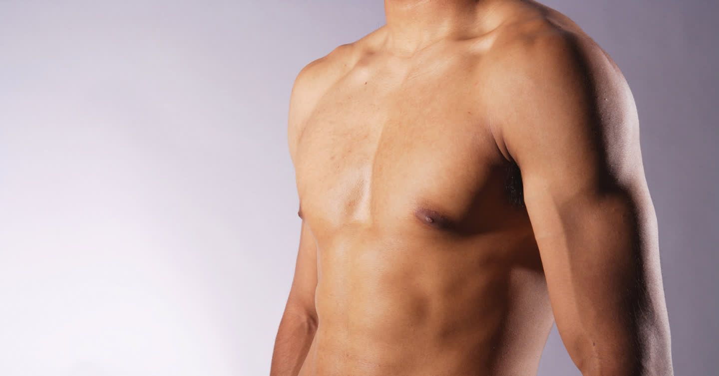 Toned male chest and torso against a grey studio background, showing results of male breast reduction