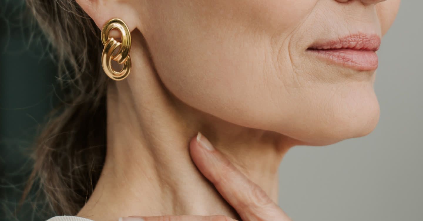 Close-up of a mature woman's lower face showing drooping mouth corners, with her hand resting on her neck