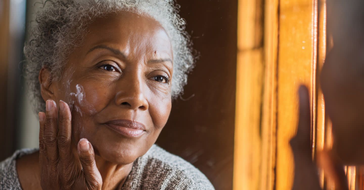 Senior woman gently touching her cheek near her nose while looking into a wooden-framed mirror