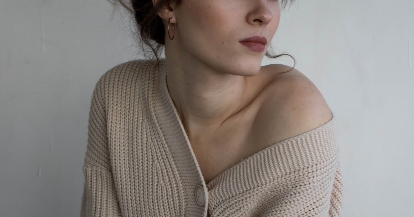 Woman with hair up wearing an off-the-shoulder beige knit cardigan, showing smooth neck and collarbone area
