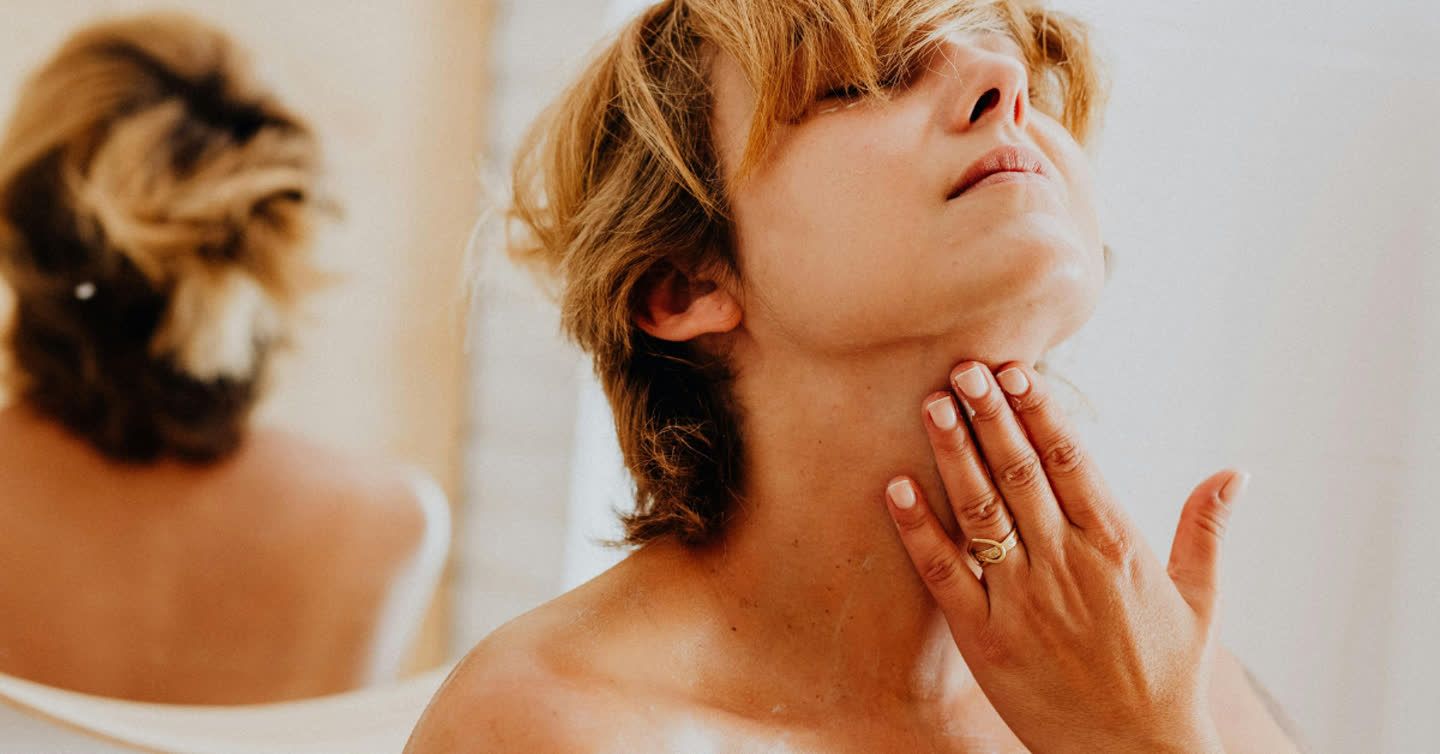 Woman tilting her head back and gently touching her neck skin while looking in a mirror