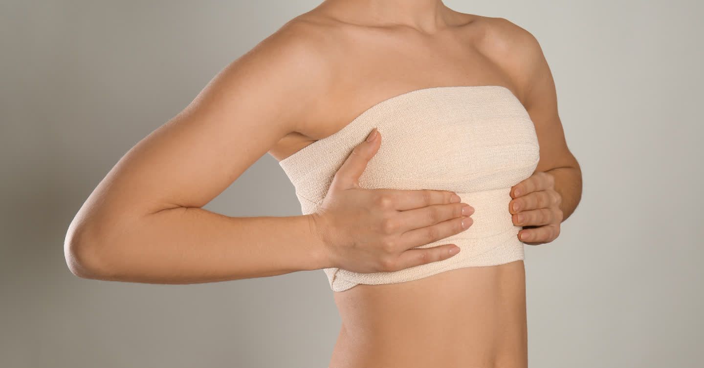 Woman with chest wrapped in surgical bandages after asymmetrical breasts correction procedure