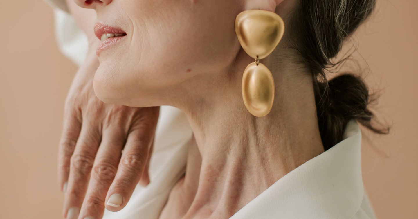 Close-up of a woman's jawline and neck with her hand resting on her chest, wearing large gold drop earrings