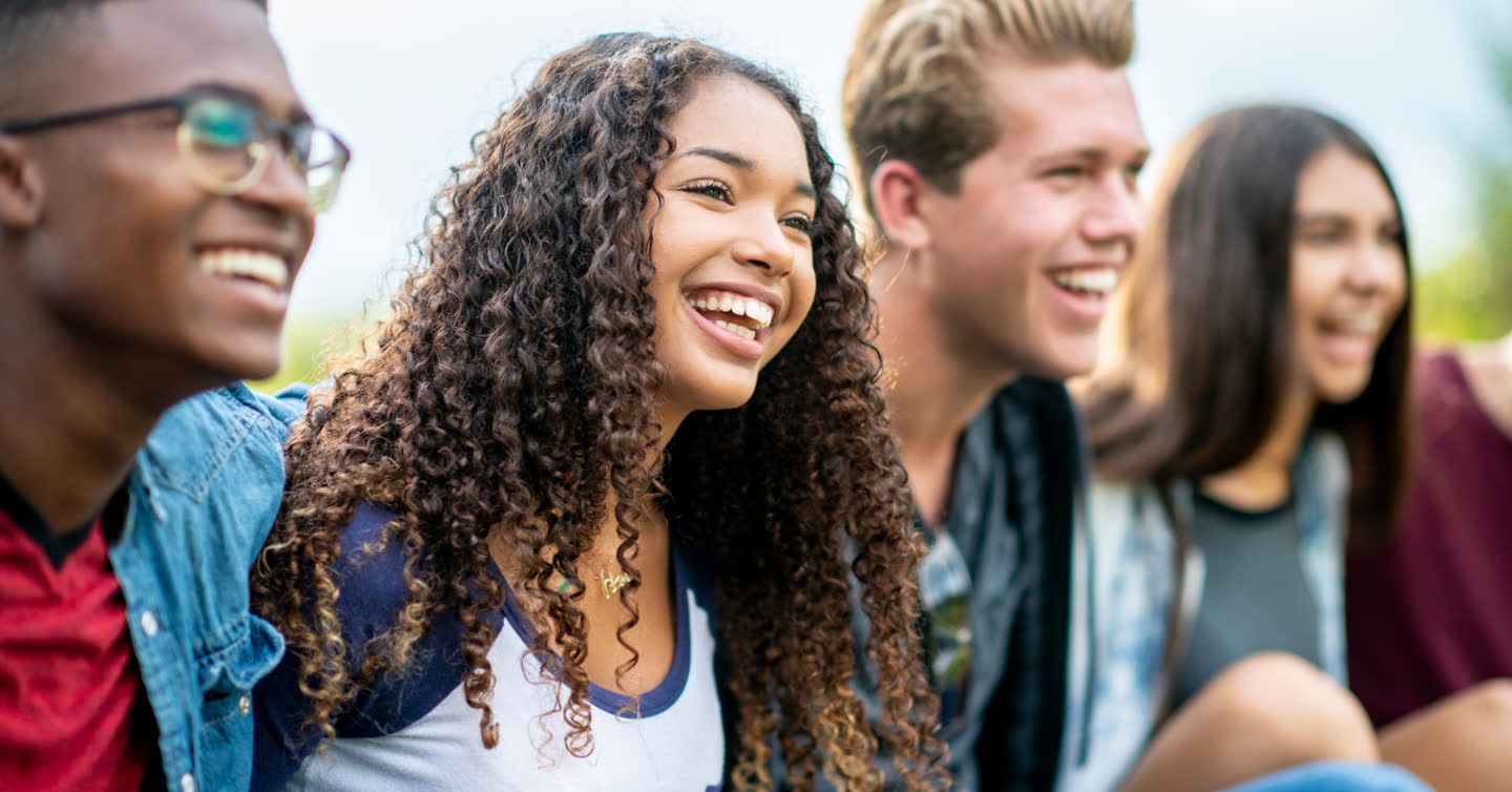 Group of diverse young people laughing together outdoors on a sunny day