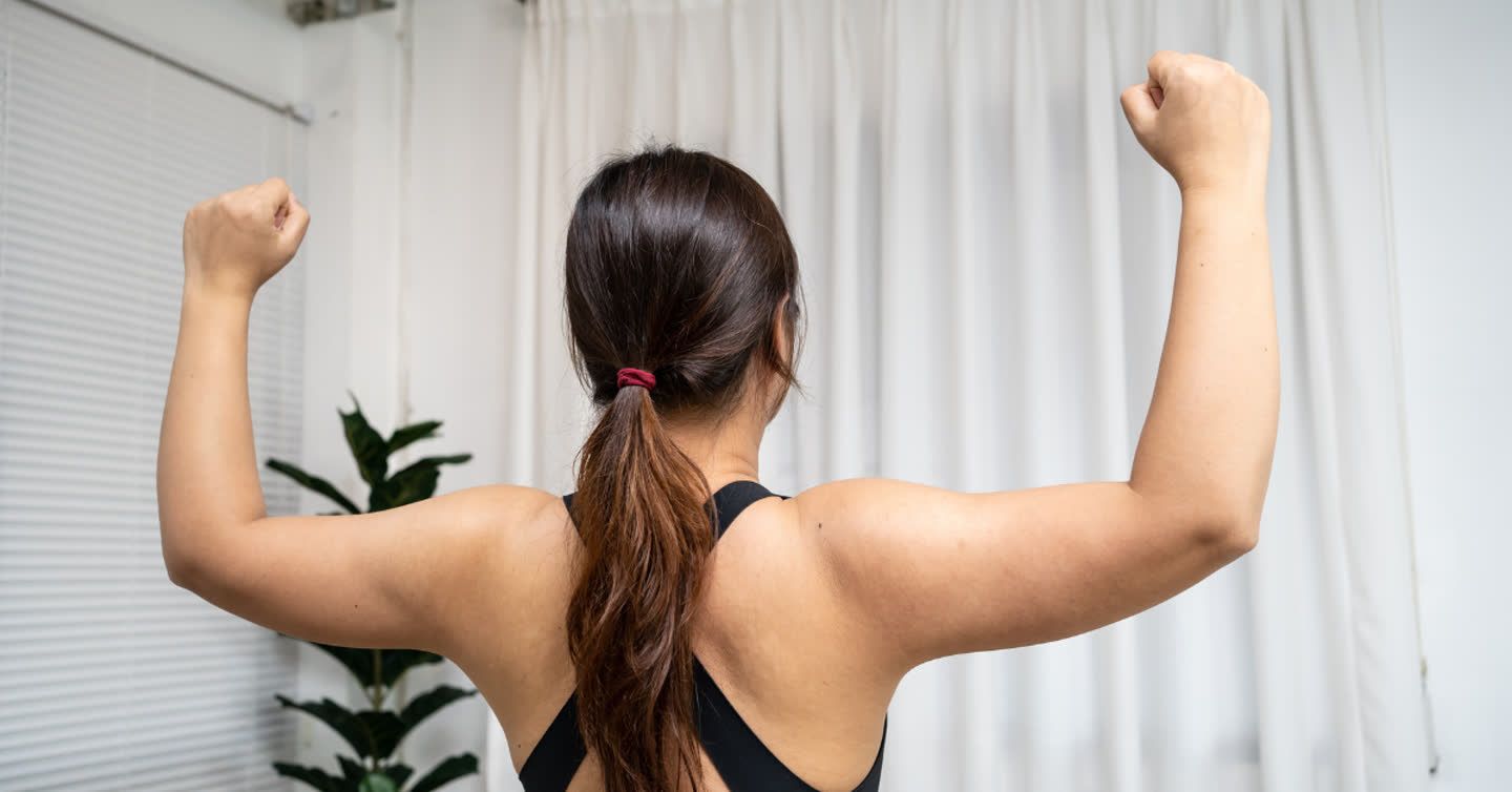 Woman seen from behind flexing both arms, showing loose skin on upper arms commonly known as bingo wings