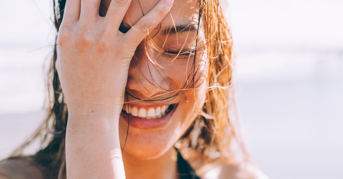 Close-up of a laughing woman covering her face with her hand, sunlight highlighting skin around her mouth