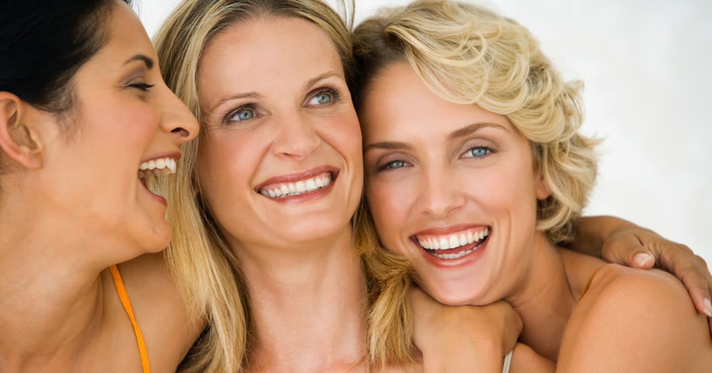 Three smiling women with radiant skin posing closely together, showing smooth neck and facial skin