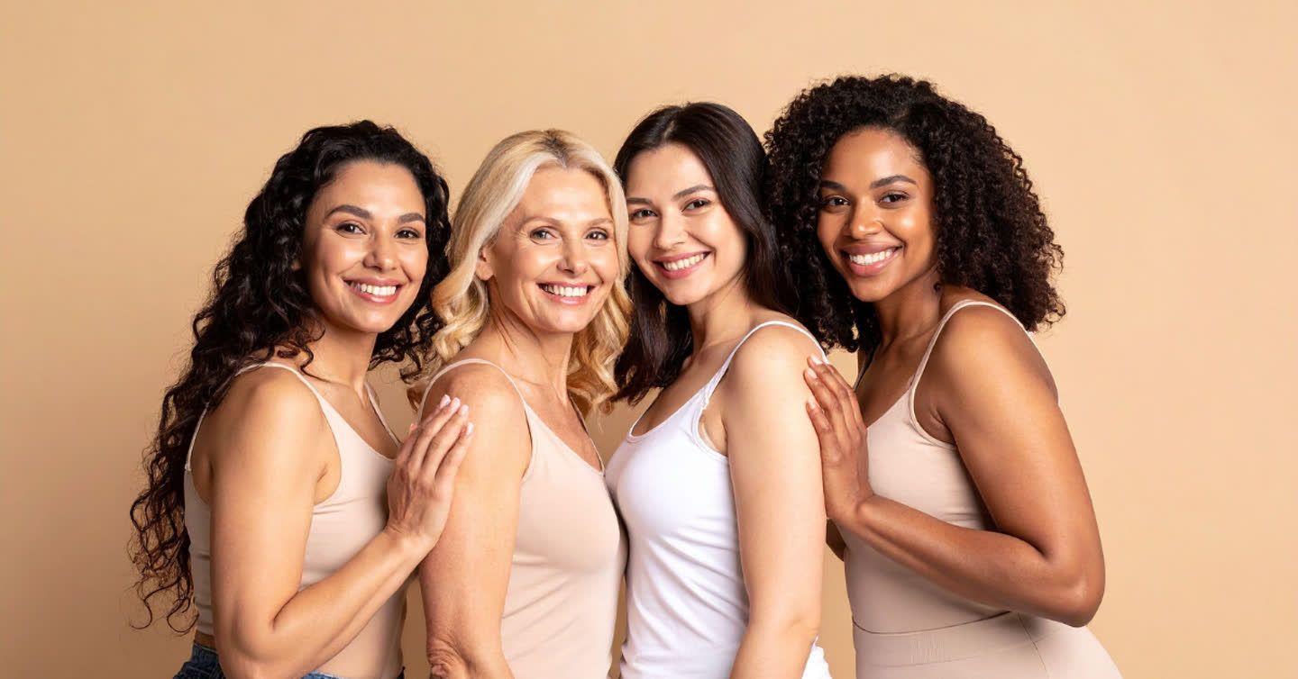Four diverse smiling women of different ages in neutral vest tops posing together against a beige background