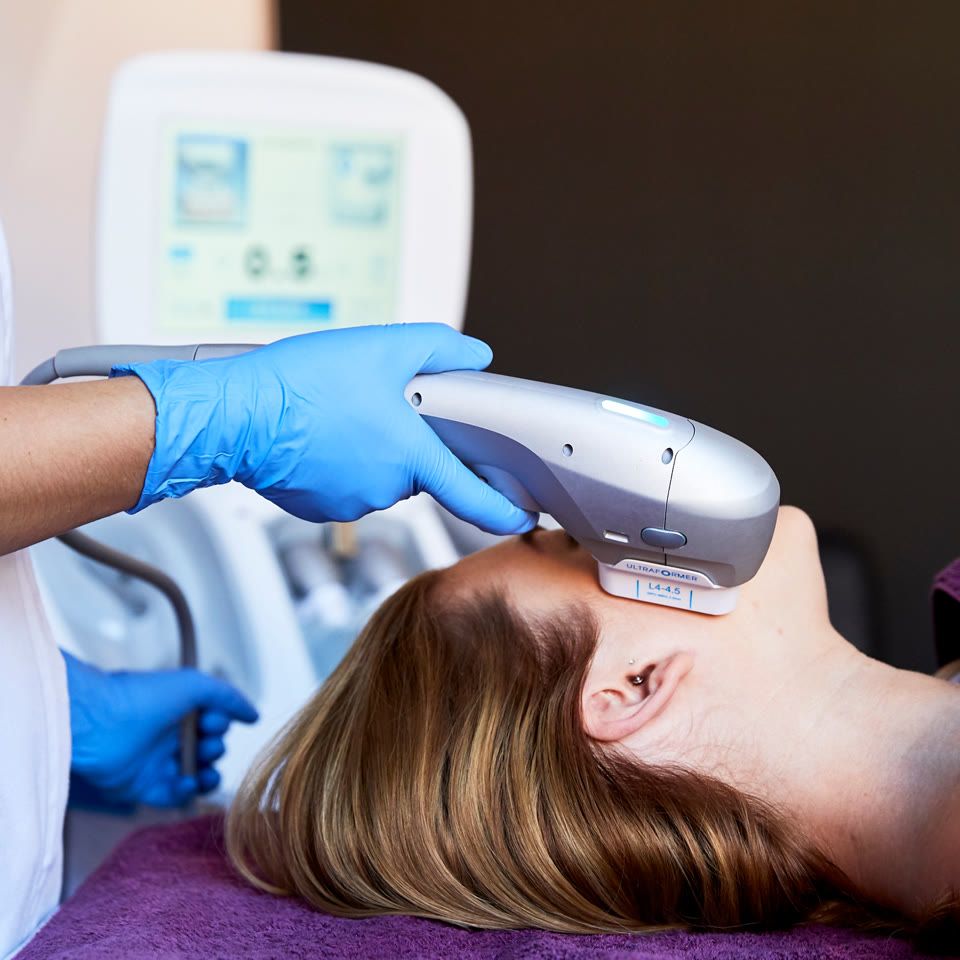Practitioner applying Ultraformer HIFU handpiece to a woman's forehead during a facial skin tightening treatment in a clinic