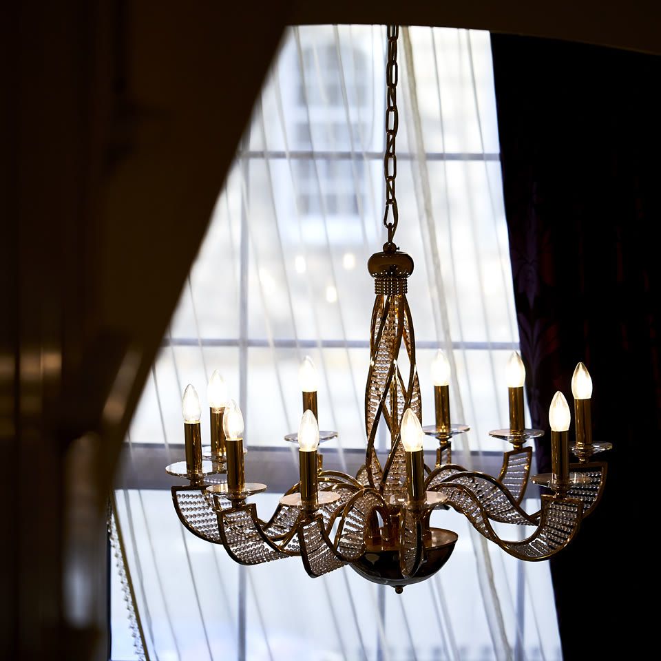 Ornate brass chandelier with candle-style bulbs hanging from a chain in front of a large arched window