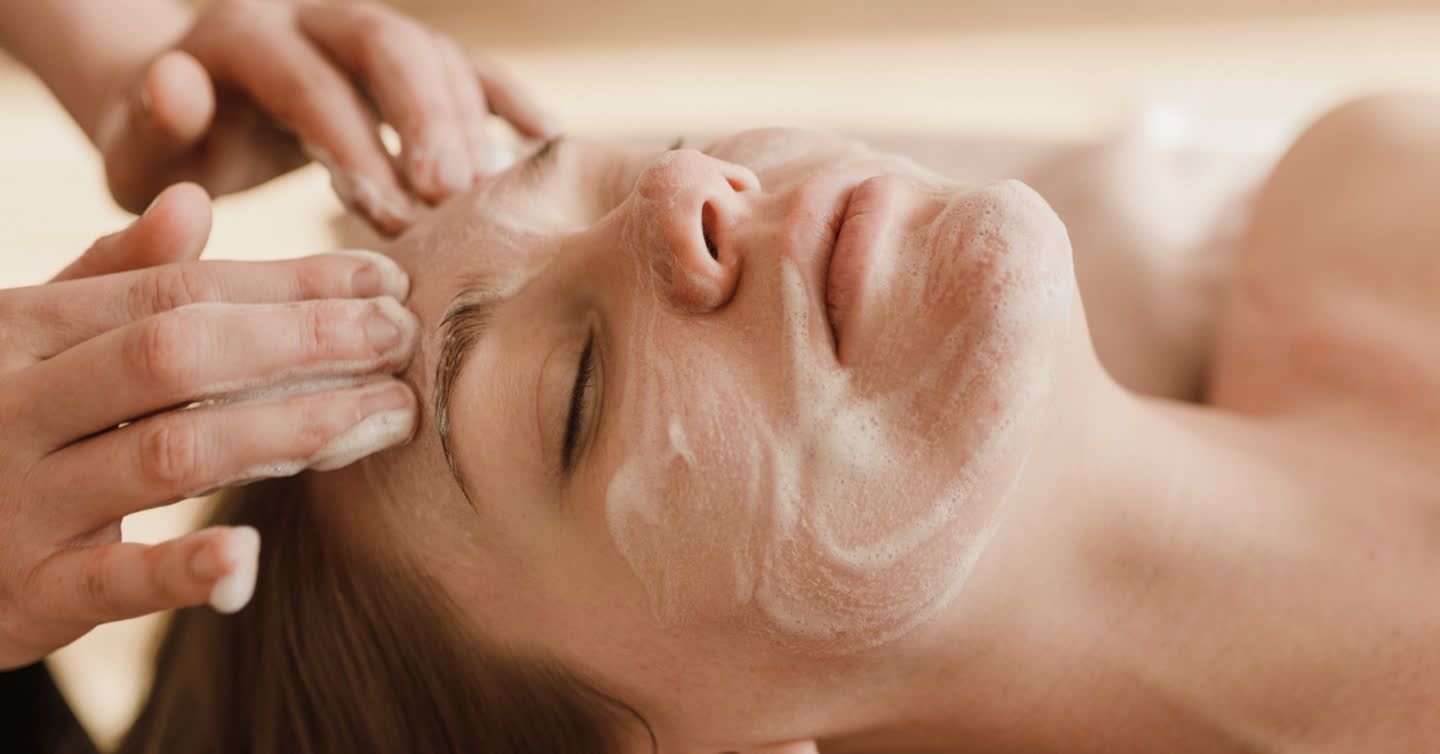 Therapist applying foaming cleanser to a woman's face during a dermamelan peel treatment at a skin clinic