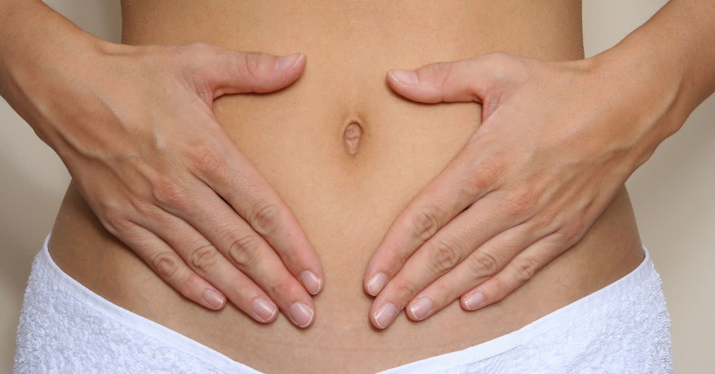 Woman holding both hands gently over her lower abdomen, wrapped in a white towel