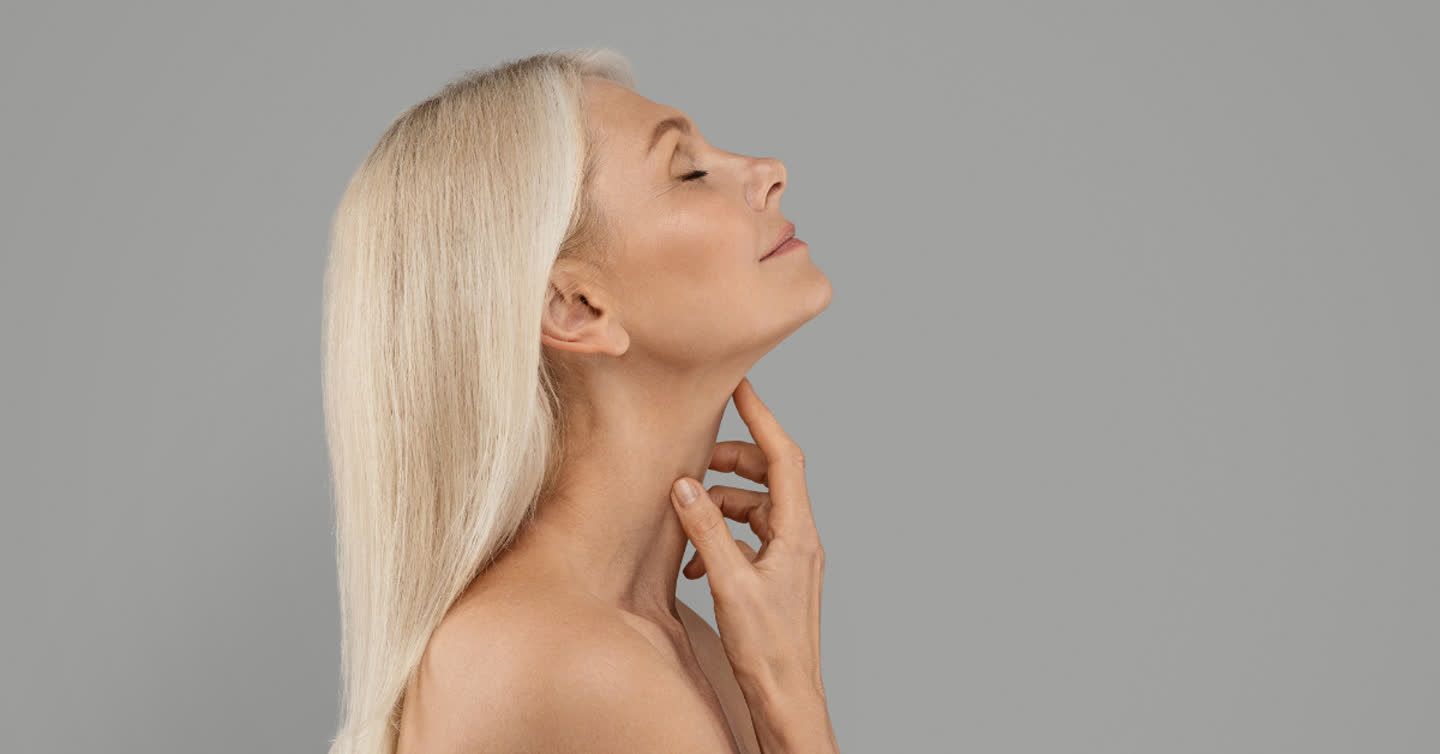 Side profile of a mature woman with long silver hair gently touching her neck, showcasing smooth radiant skin