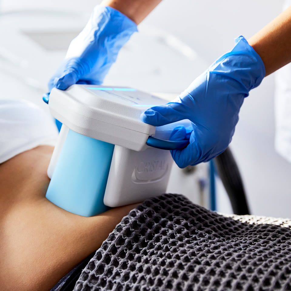 Practitioner in blue gloves applying an LPG Endermologie device to a patient's abdomen during a treatment session