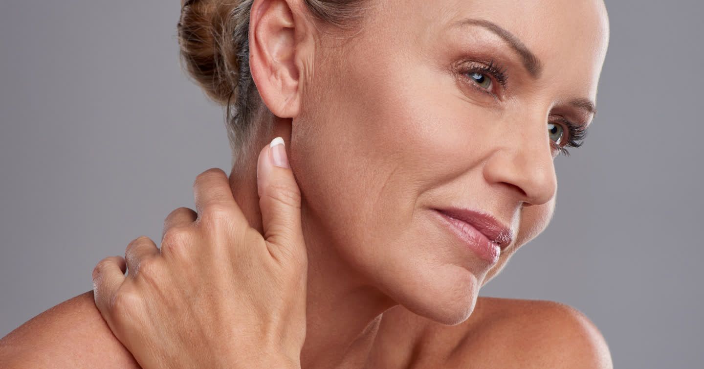 Mature woman gently touching her neck and jawline, showcasing smooth skin after a neck lift