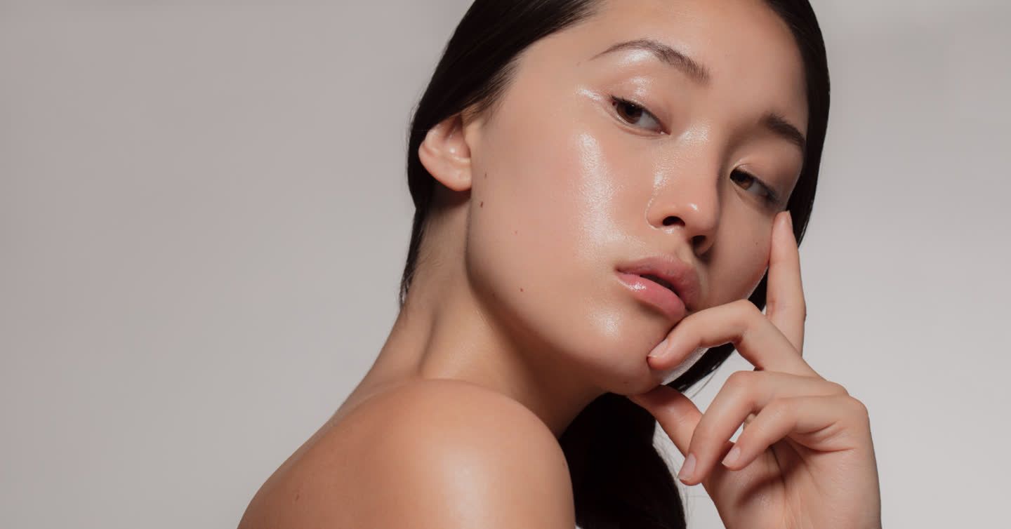 Close-up of a young woman with glowing skin resting her hand gently against her chin and nose