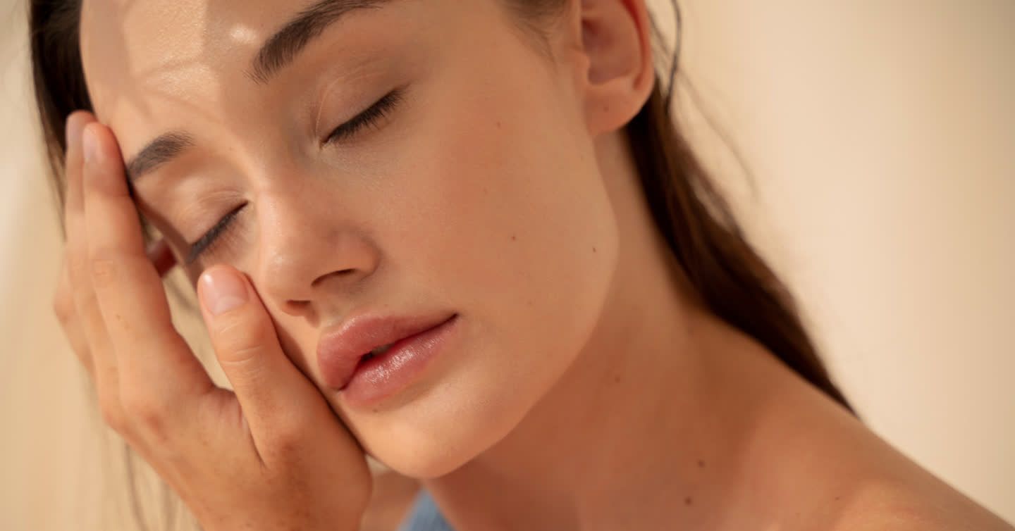Close-up of a woman with eyes closed gently touching her smooth, glowing skin after Fraxel laser treatment