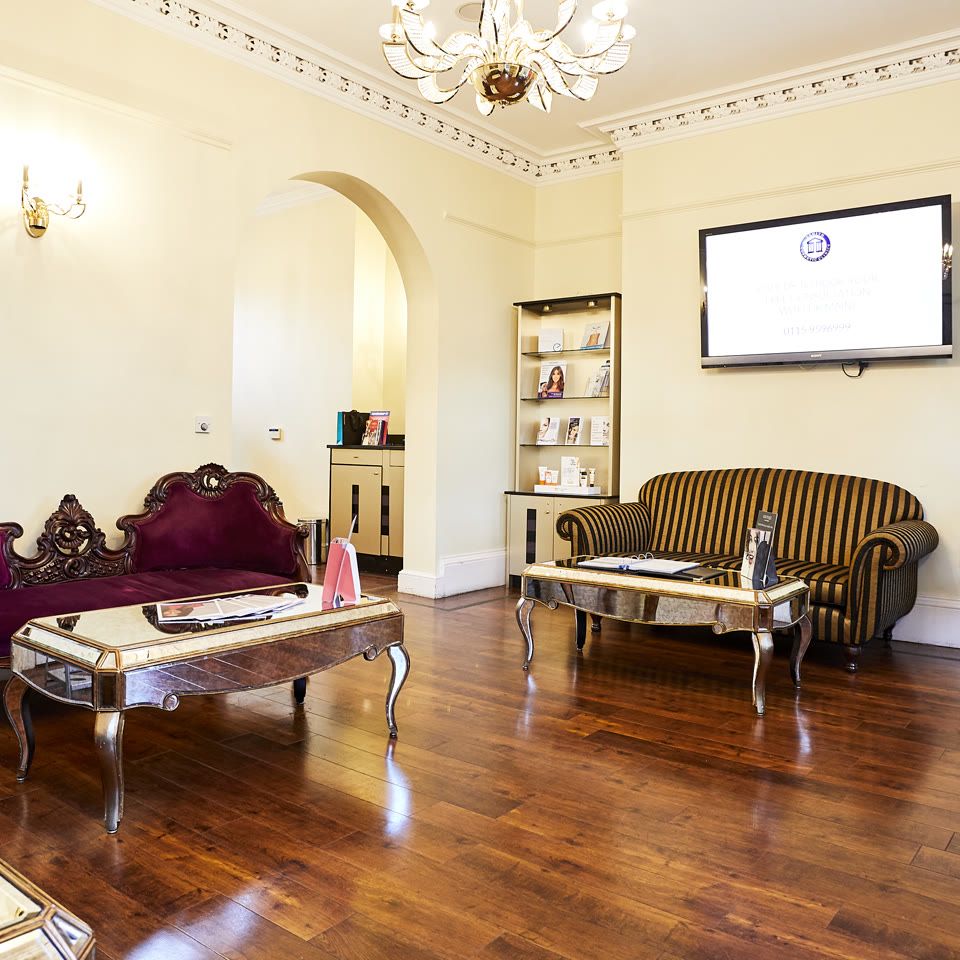 Elegant clinic waiting room with ornate velvet sofa, striped settee, mirrored coffee tables, and polished wooden floors
