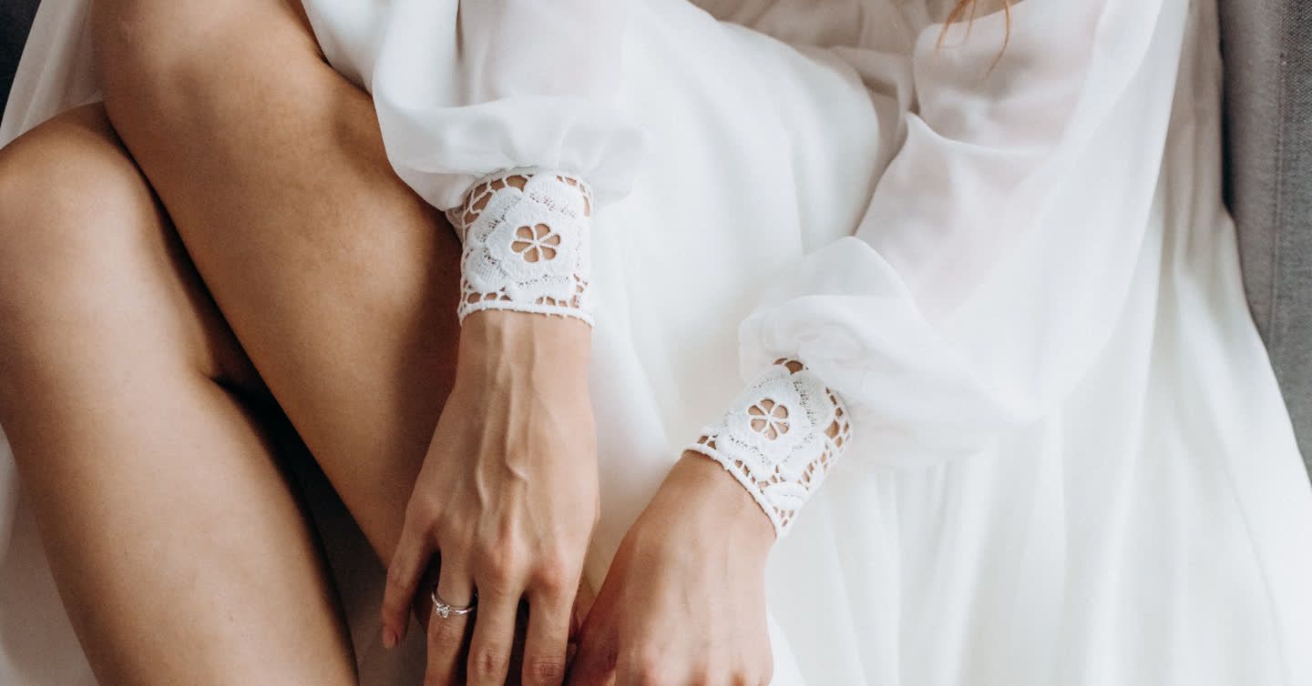 Close-up of a woman's hands and legs wearing a white dress with floral lace cuffs and an engagement ring