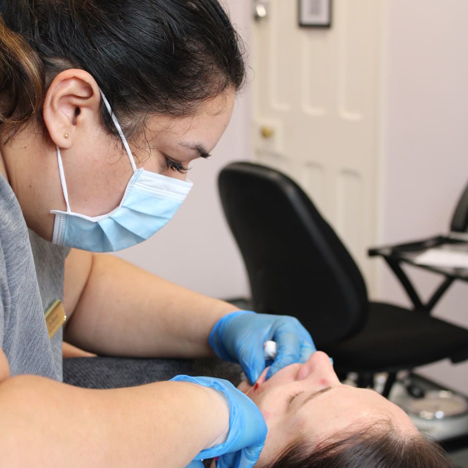 Practitioner wearing a face mask and blue gloves administering a dermal filler injection to a client's face during an 8-point facelift treatment