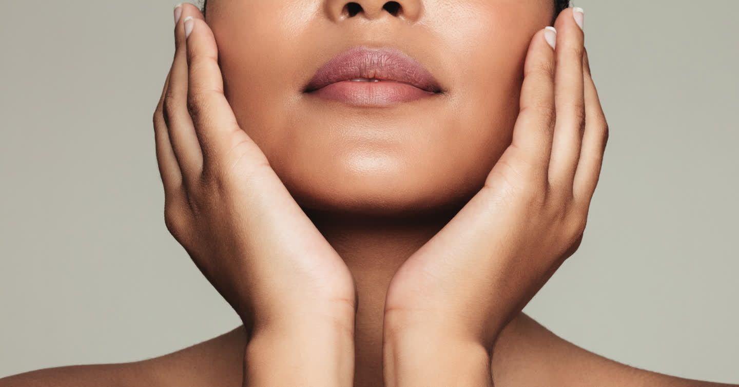 Woman gently cradling her smooth, clear face with both hands, showing radiant skin and mauve lipstick