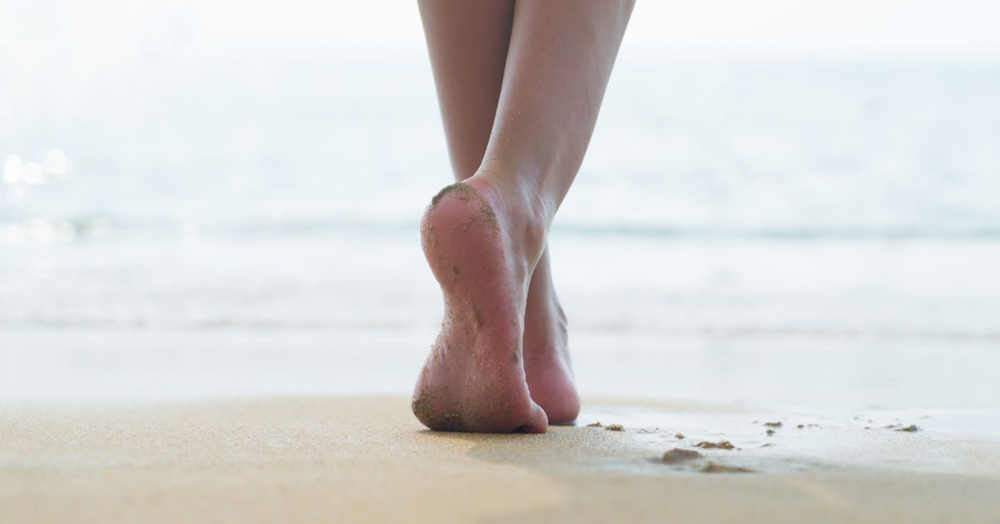 Bare feet walking on wet sandy beach with close-up view of heels and soles