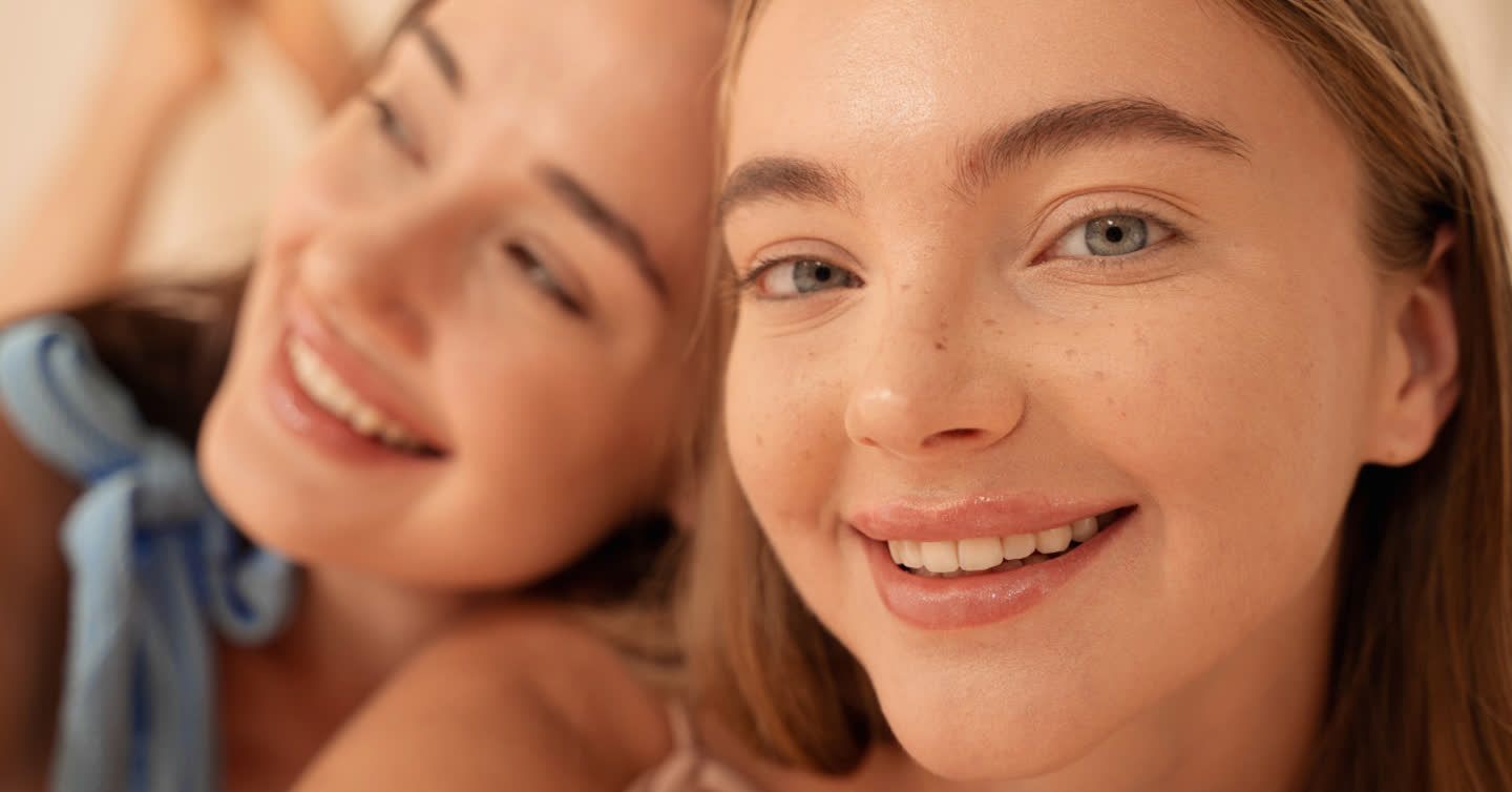 Close-up of two smiling young women with natural makeup, smooth skin, and naturally thin lips