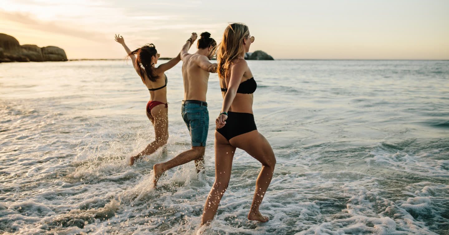 Three friends running into the ocean waves at sunset on a sandy beach